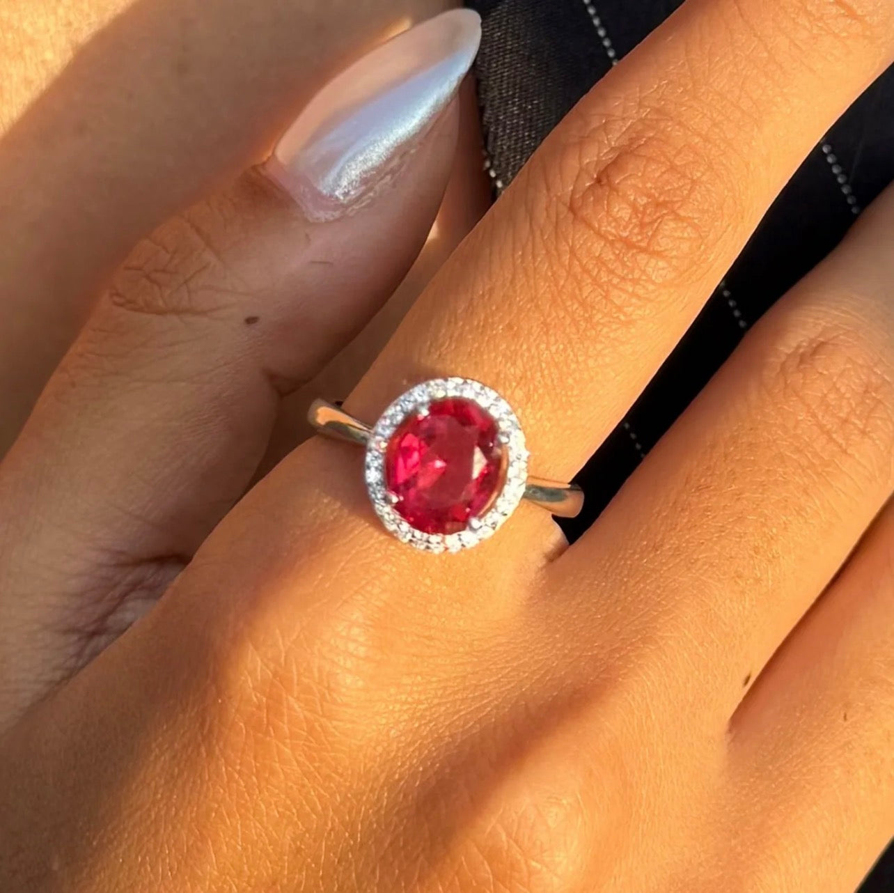 Woman wearing a ruby-red oval CZ halo silver ring
