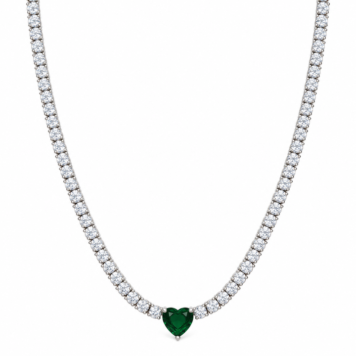 A tennis-style necklace with a heart-shaped green gemstone pendant, set in a silver-toned metal with a row of clear stones along the chain, shown against a plain white background.